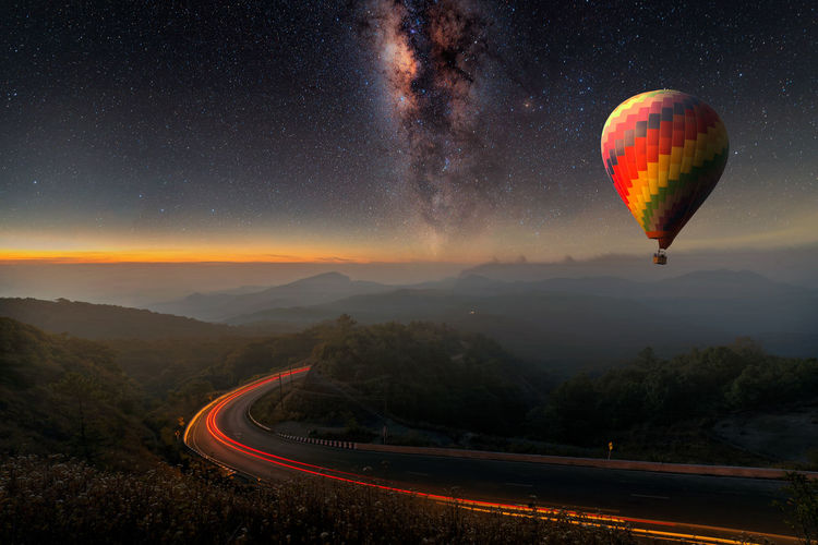 Hot air balloon flying over landscape against dramatic sky at night