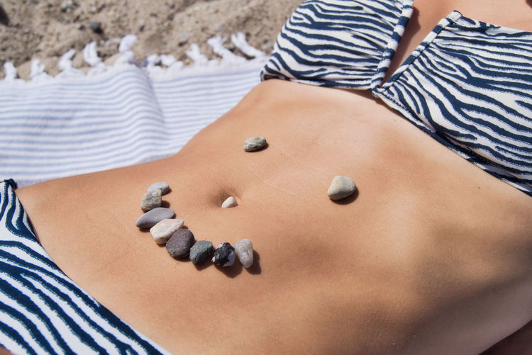 Midsection of woman with pebbles on stomach at beach