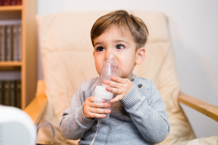 Boy looking away while inhaling through respiratory mask at home