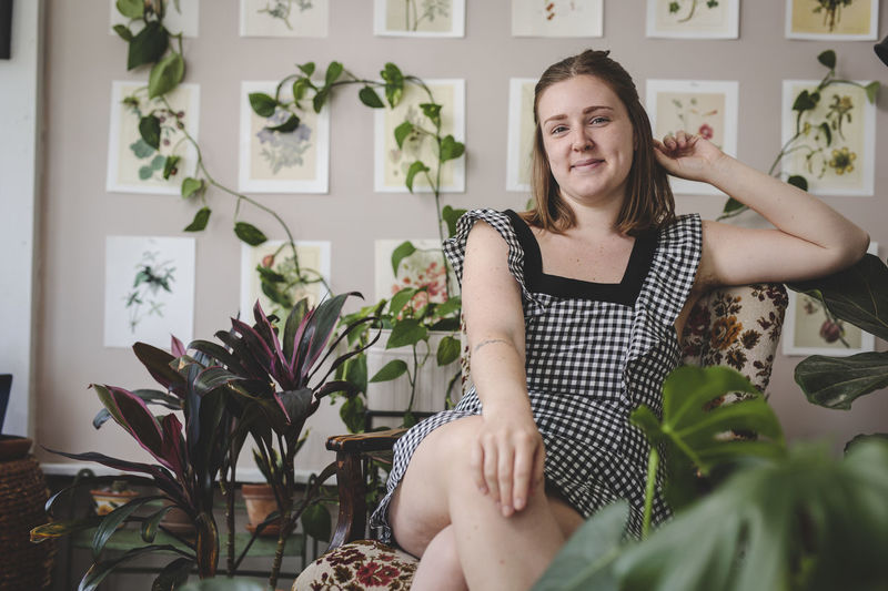 Stylish young woman smiles while sitting in chair with plants