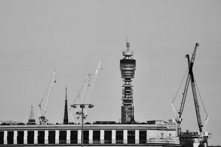 Cranes on pier amidst buildings against clear sky