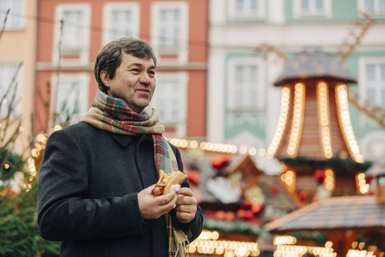 Smiling mature man standing with hot dog at christmas market