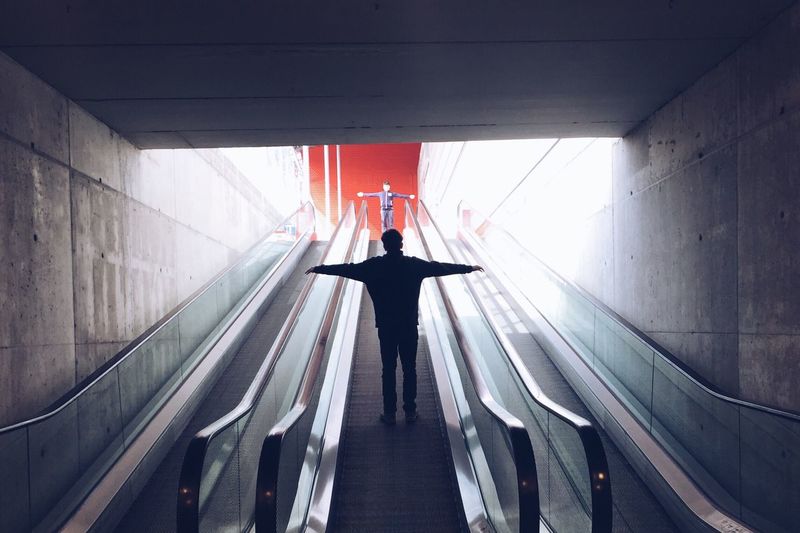People with arms outstretched while standing on escalator