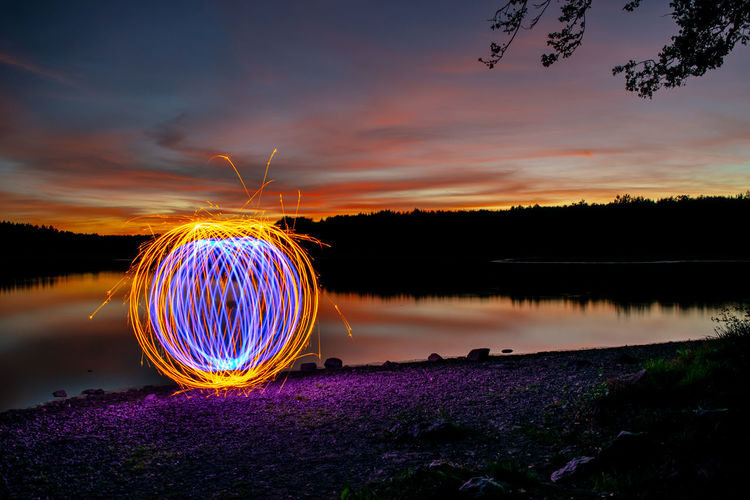 Illuminated ferris wheel in lake against sky at sunset