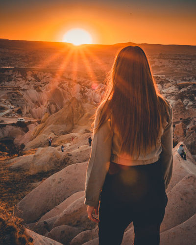 Rear view of woman standing on land against sky during sunset
