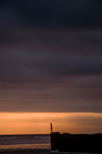Silhouette person standing on cliff against sea during sunset
