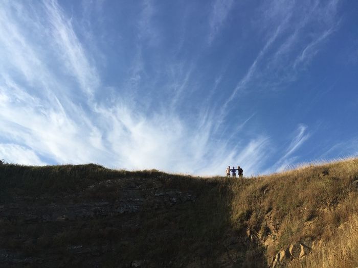 Low angle view of friends standing on hill against sky
