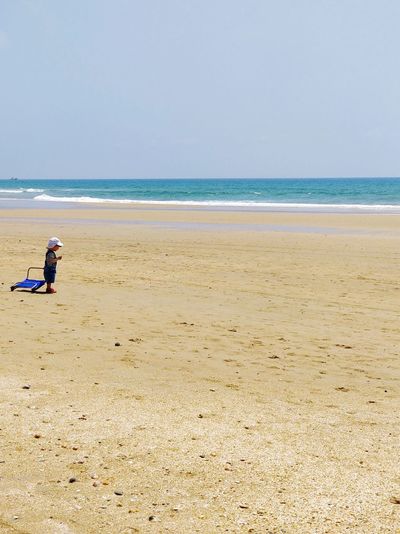 Mid distance view of boy standing at beach against clear sky