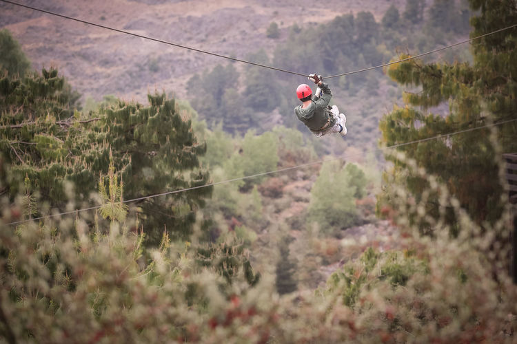 Rear view of person hanging on steel cable over landscape