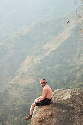 Side view of young man sitting on mountain