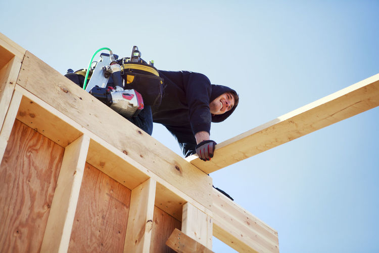 Low angle view of smiling worker making construction frame against clear blue sky