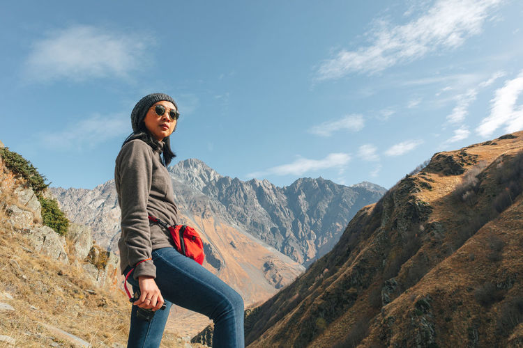Low angle view of woman wearing sunglasses standing on mountain against sky