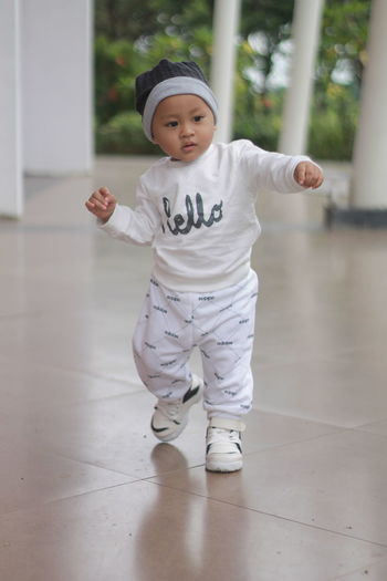 Cute and adorable toddler with a cute smile while standing on the floor in a sporty white costume
