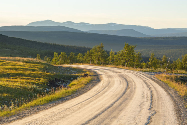 Dirt road with a scenic view of a woodland with mountains in the horizon