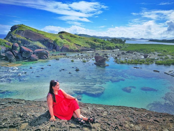 Woman sitting on rock by sea against sky
