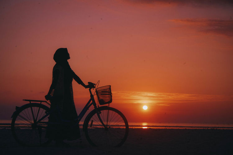 Silhouette man on bicycle at beach during sunset