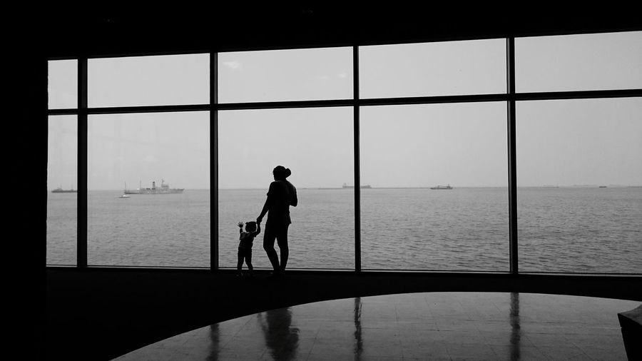 Silhouette mother holding child standing next to glass window