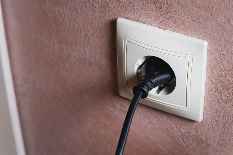 Electric socket on a pink wall. the black wire plug is connected. renovated backdrop of studio