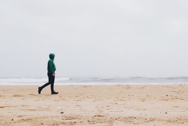 Man walking on shore at beach against sky