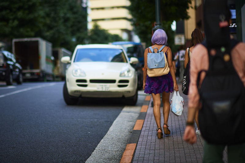 People walking on sidewalk by cars in city