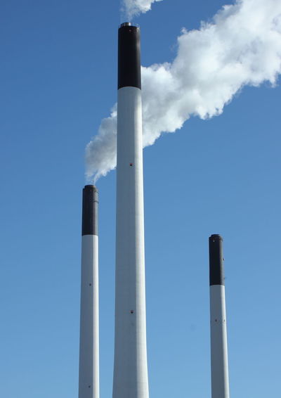 Low angle view of smoke stacks steaming against clear sky
