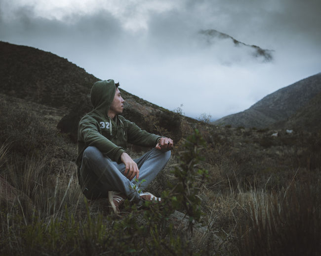 Young man sitting on rock admiring mountains with low clouds