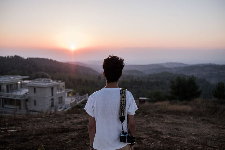 Rear view of man with camera looking at view while standing on mountain against sky