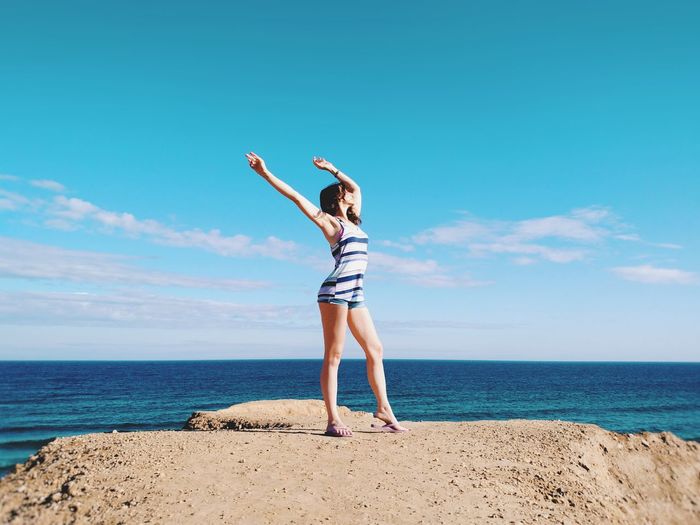 Young woman with arms raised standing at beach against sky during sunny day