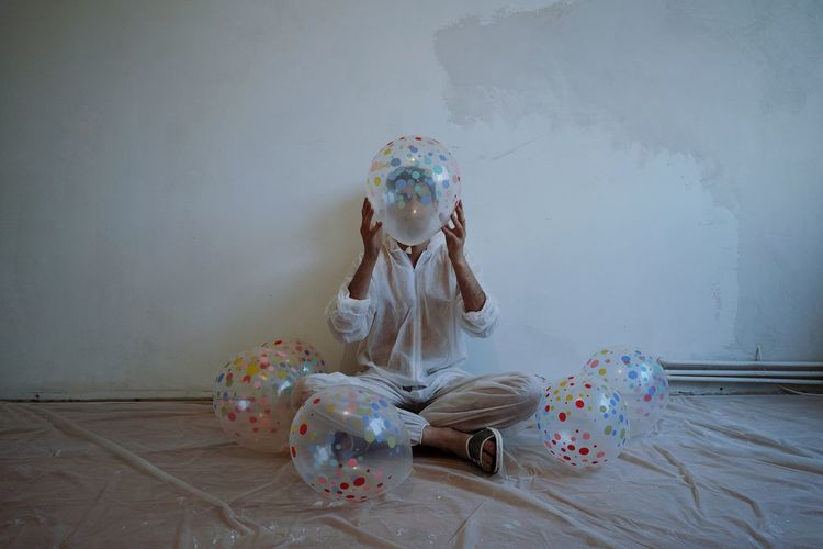 Man covering face with balloon while sitting against wall