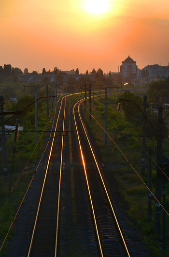 Railroad tracks in city against sky during sunset