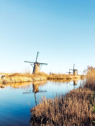 Traditional windmill by lake against clear sky