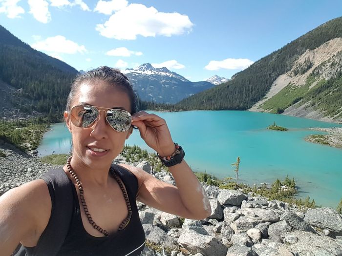 Portrait of woman wearing sunglasses while standing against lake amidst mountains