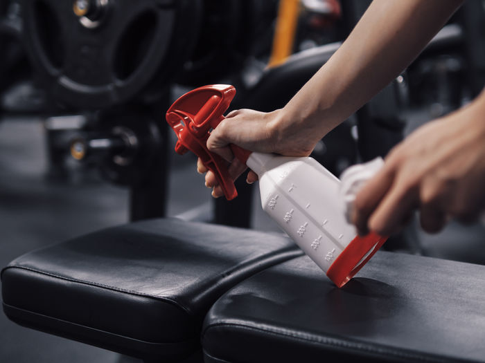 Cropped hand of woman cleaning seat in gym
