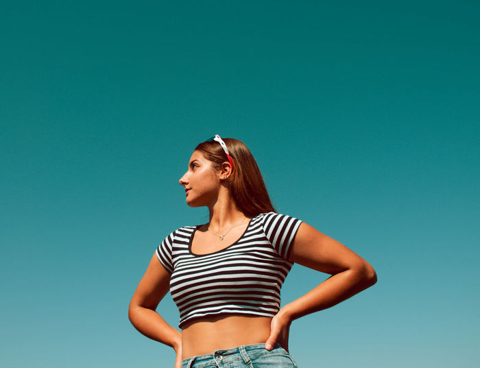 Young woman looking away against blue sky