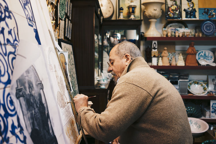 Side view of senior master working with ceramic tile on paint easel