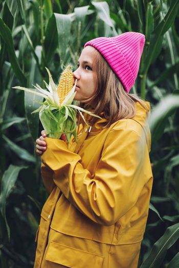Funny little girl dressed in a yellow raincoat and a hot pink cap spoils and bites corn 