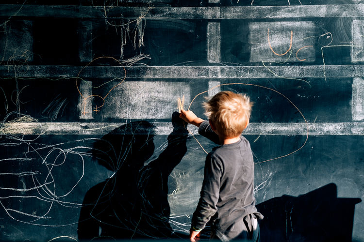 Rear view of boy writing on blackboard