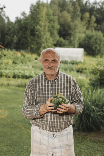 Portrait of content senior man with handfull of cucumbers in his garden