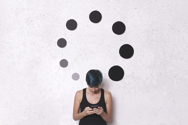Woman using phone while standing by circular shape decorations on wall