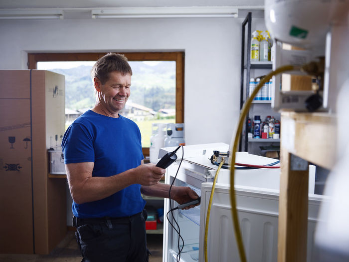 Smiling male electrician holding equipment while checking temperature at workshop