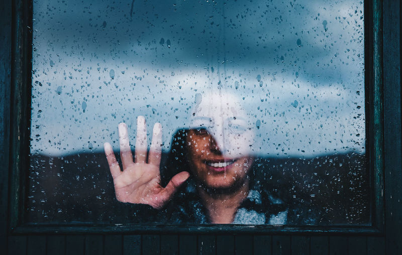Close-up of woman on wet window in rainy season