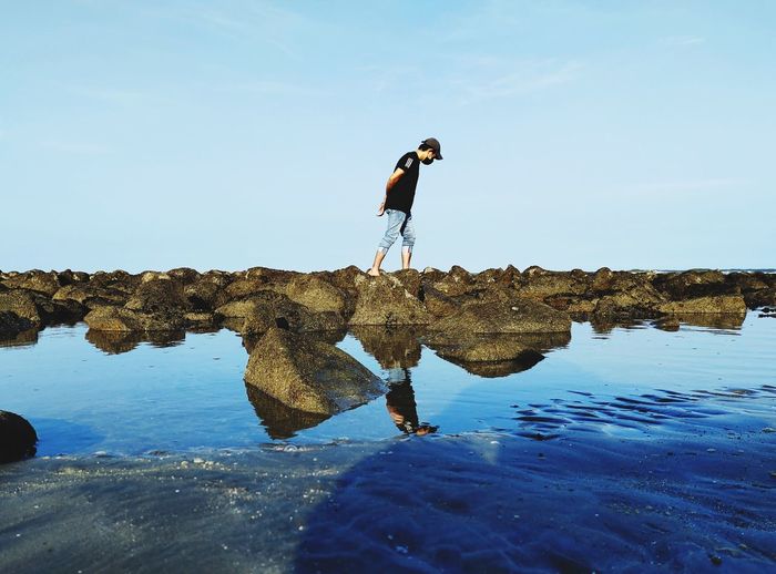 Man standing on rock against sky