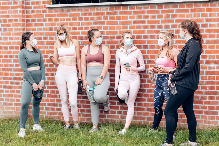 Group of six women in sportswear gathering together outside the gym wearing protective medical mask