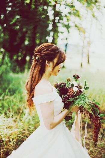 Side view of woman holding bouquet while standing outdoors