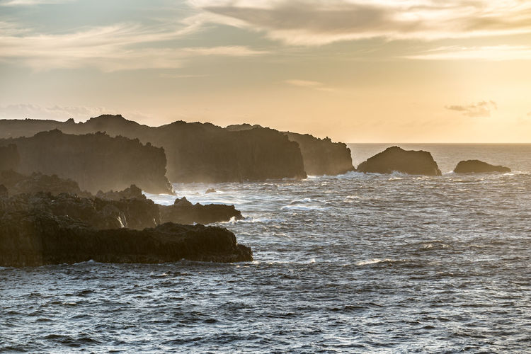 Rock formations in sea against sky during sunset