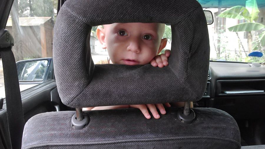 Portrait of boy looking though seat while traveling in car