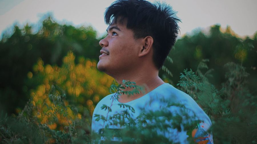 Portrait of young man looking away against plants