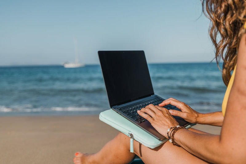 Midsection of woman using laptop at beach