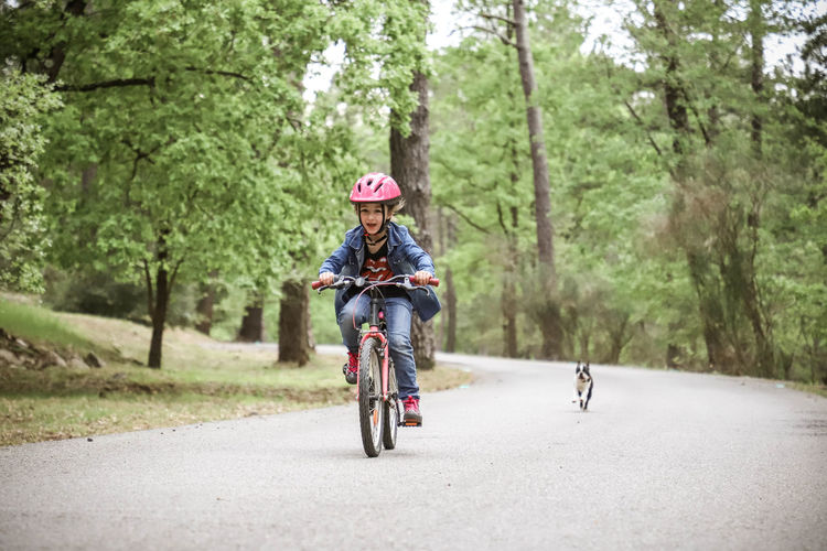 Girl riding bicycle while dog running on road in forest