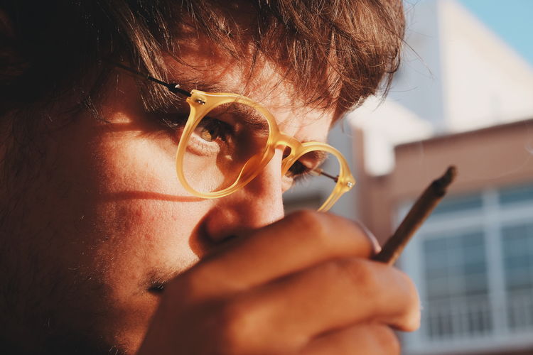 Close-up of man wearing eyeglasses holding joint